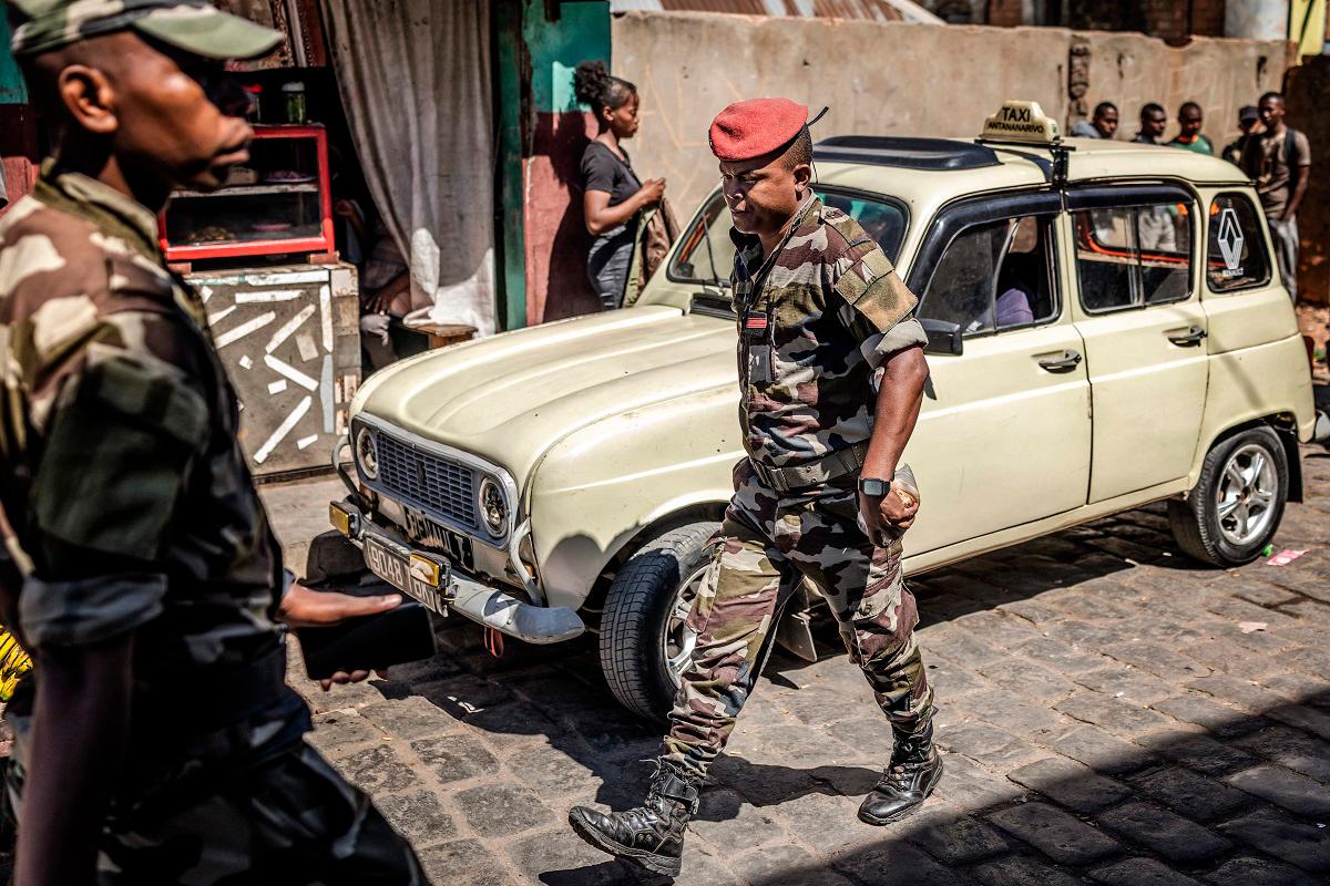 Members of Madagascar’s Army CAPSAT unit walk past an old taxi near the CAPSAT base, a day after the unit announced it would assume power in Antananarivo, on October 15, 2025. - Luis TATO / AFP