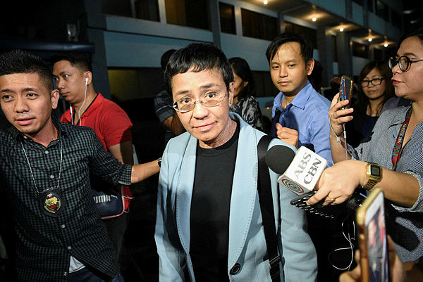Philippine journalist Maria Ressa (C) is surrounded by the press as she is escorted by a National Bureau Investigation (NBI) agent (L) at the NBI headquarters after her arrest in Manila — AFP