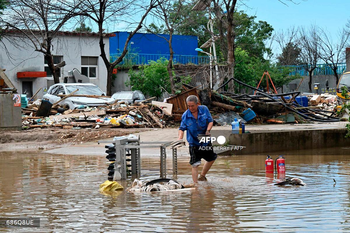 A man salvages items in a flooded area in Miyun district, northern Beijing on July 29, 2025. Heavy rain in Beijing killed 30 people and forced authorities to evacuate tens of thousands as swathes of northern China were lashed by torrential downpours that sparked deadly landslides, state media said on July 29. - ADEK BERRY / AFP
