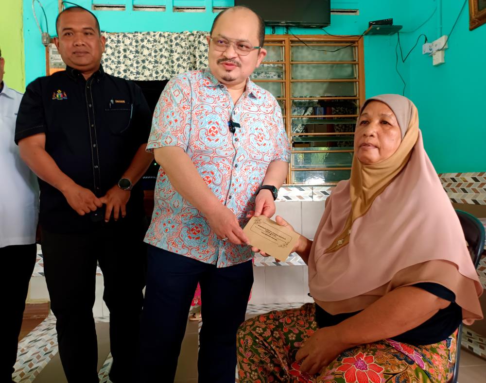 Setiausaha Politik Kanan Perdana Menteri Datuk Seri Shamsul Iskandar Mohd Akin (tengah) menyampaikan sumbangan kepada penerima Aminah Ahmad, 65, pada program penyerahan Sumbangan Kecemasan Perdana Menteri Kepada Mangsa Bencana Banjir di Kampung Bukit Balai, Durian Tunggal di sini hari ini/BERNAMAPix