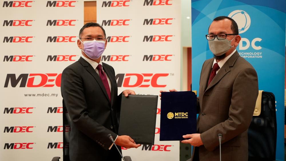 Mahadhir (left) and Norhalim exchanging the signed MoU between MDEC and MTDC on April 11.