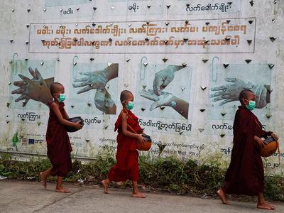 Buddhist novice monks wearing face masks walk past a Covid-19 awareness sign as they collect morning alms, in Yangon, Myanmar. -AP