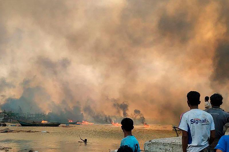 This handout photo taken and released on January 9, 2025 by the Arakan Army (AA) ethnic minority armed group shows people looking at burning homes at the site of a suspected air strike carried out by Myanmar’s military at Kyauk Ni Maw village in Ramree island in western Rakhine State. A Myanmar junta air strike killed at least 40 people in a town in western Rakhine state, a rescue worker and ethnic minority armed group told AFP on January 9, 2025. - AFP PHOTO / ARAKAN ARMY (AA)