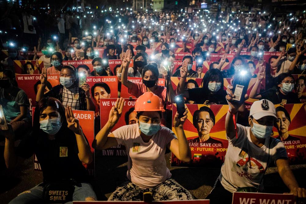 (FILES) In this file photo taken on March 12, 2021, protesters hold up the three finger salute and placards with the image of detained Myanmar civilian leader Aung San Suu Kyi while using their mobile torches during a demonstration against the military coup in Yangon. This August 1, 2021 marks six months since Aung San Suu Kyi, the daughter of independence hero Aung San, was detained in a coup by the military her father created, setting off a bloody crackdown that has killed hundreds. - AFP