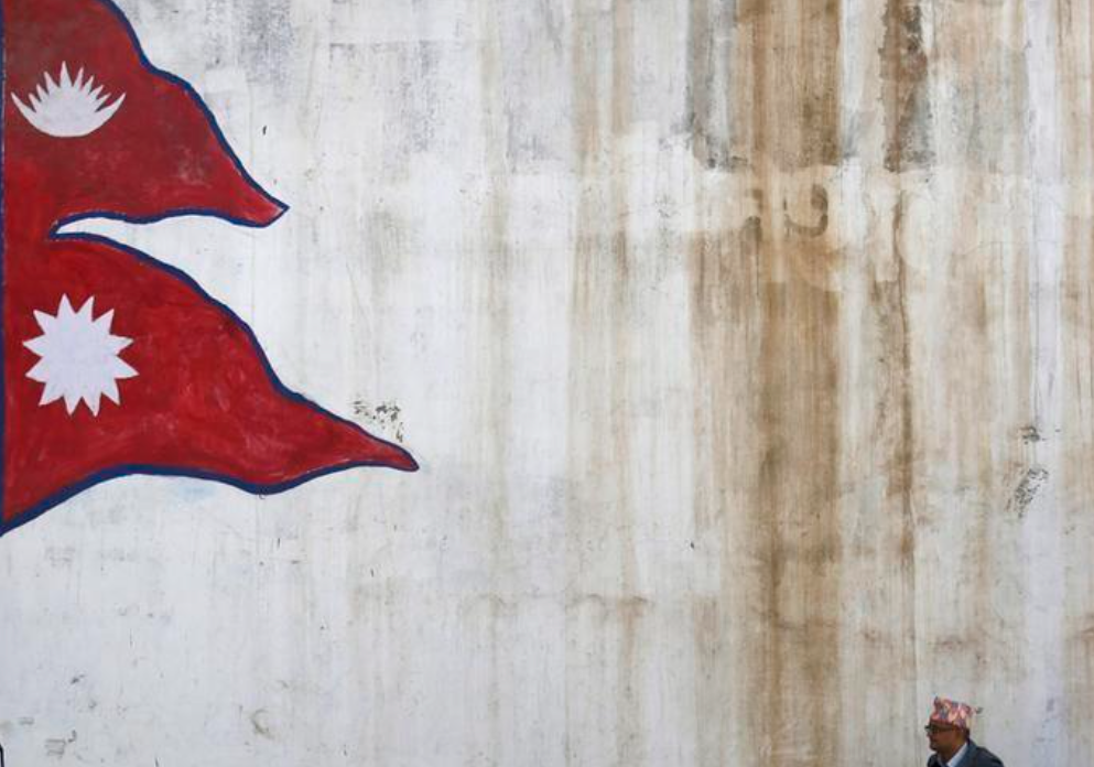 A man stands near a wall with a painting of a Nepali national flag as he waits for a bus in Kathmandu, Nepal October 16, 2015. REUTERSPIX