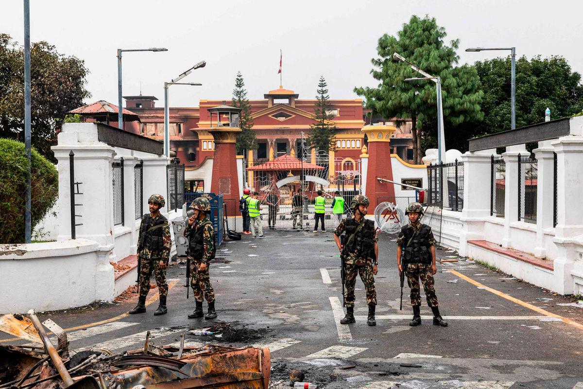 Army personnel stand near charred remains as they patrol along a street outside the torched President House in Kathmandu on September 10, 2025. Nepali soldiers patrolled the streets of Kathmandu on September 10, seeking to restore order after protesters set parliament ablaze and forced the prime minister to quit in the worst violence to hit the Himalayan nation in two decades. (Photo by PRABIN RANABHAT / AFP)