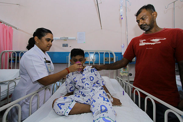 Port Dickson Hospital nurse who is also mother to R. Deshwindran (center), 9, feeds him a drink after being being admitted at the children’s ward of Port Dickson Hospital along with six others today.