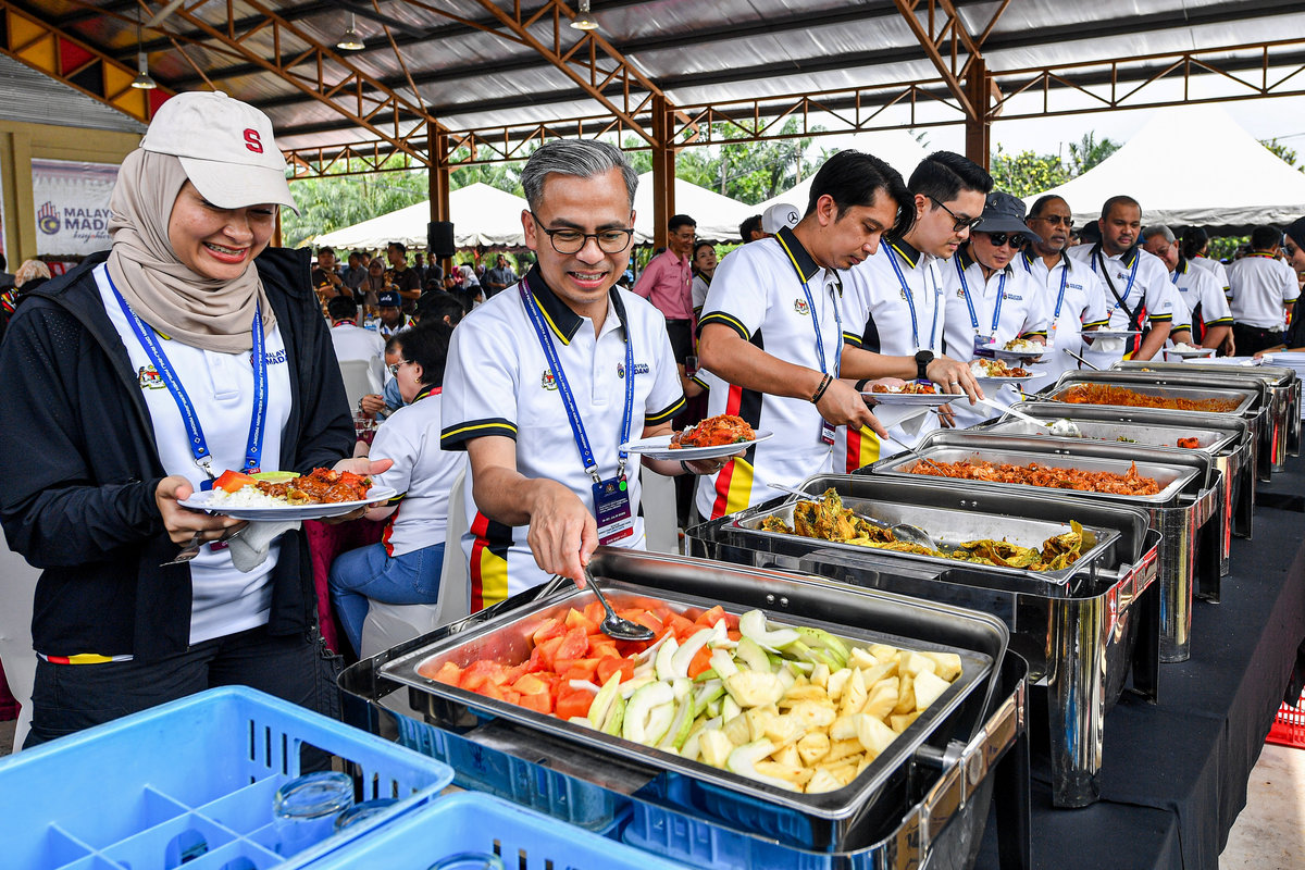 Menteri Komunikasi Datuk Fahmi Fadzil (dua, kiri) mengambil juadah yang dimasak secara gotong-royong oleh penduduk setempat pada Program Ukhwah Kepimpinan MADANI di Dataran Kampung Pachitan hari ini. - BERNAMA