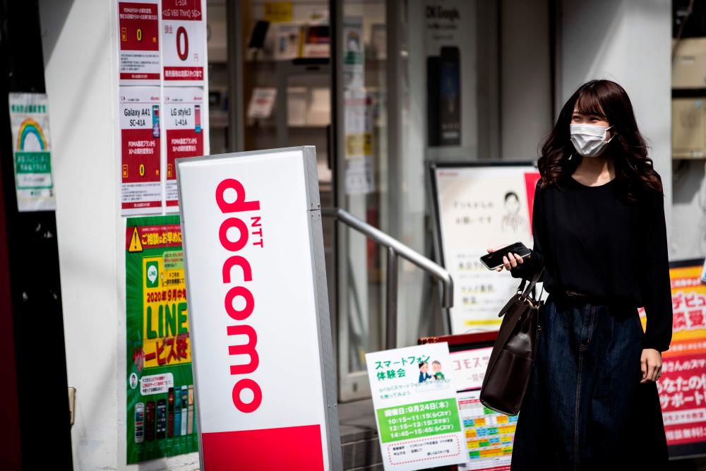 A woman walking past a store of NTT Docomo in Tokyo on Tuesday. NTT's share price fell as much as 5.8% after the company said it was considering a buyout of its wireless unit. The stock closed down 3% while NTT Docomo ended up 16% at its daily trade limit.. – AFPPIX