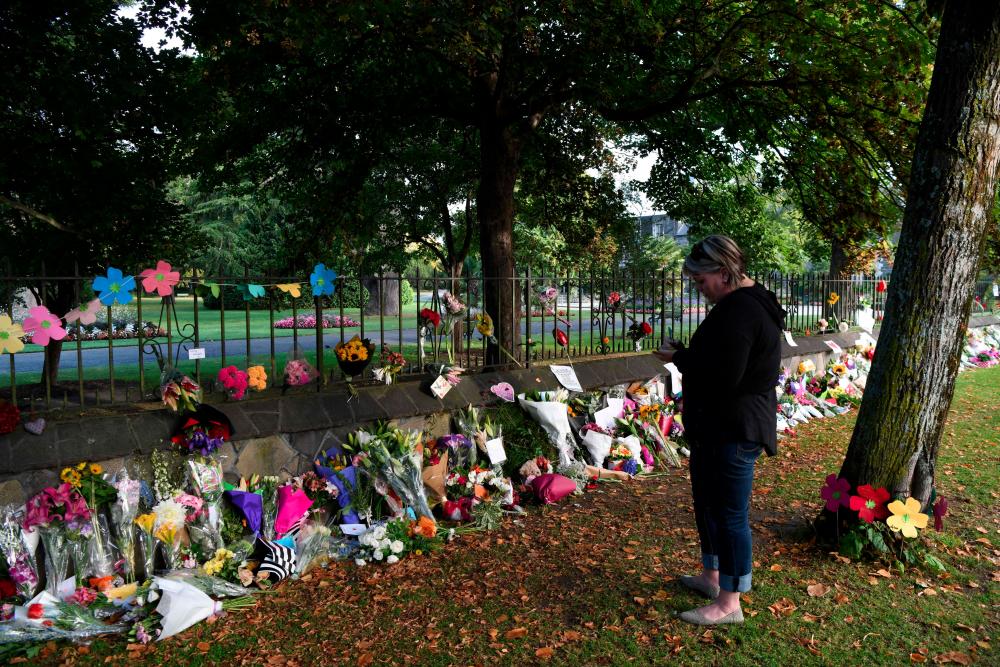 A woman writes a note to leave among flowers left in tribute to victims in Christchurch on March 17, 2019, two days after a shooting incident at two mosques in the city. — AFP