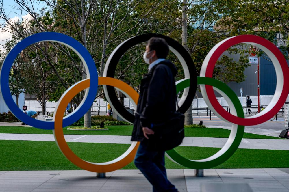 A man wearing a face mask walks in front of the Olympic Rings in Tokyo on March 11, 2020. - AFP