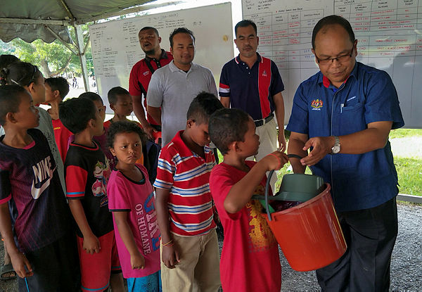 Hashim Alang Abd Hamid (R) giving out essential self cleaning products to the Orang Asli Children — Bernama