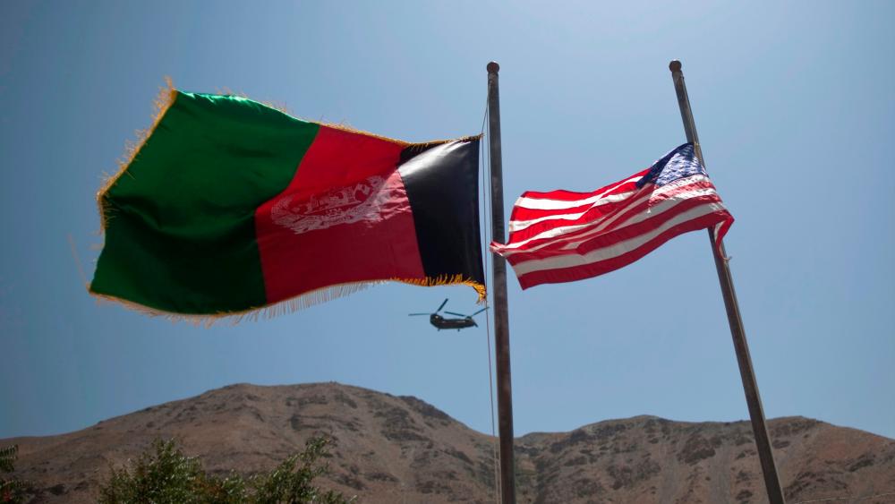 An Afghan flag flutters next to a U.S. flag as a U.S Chinook helicopter flies over Panjshir province on July 24, 2011. -Reuters