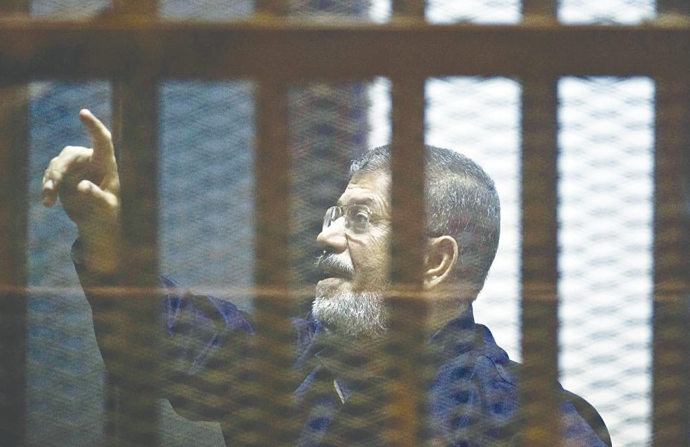 Morsi stands behind bars during his trial on June 16. Under international humanitarian law any sudden death in custody must be followed by an independent investigation. – AFPpix