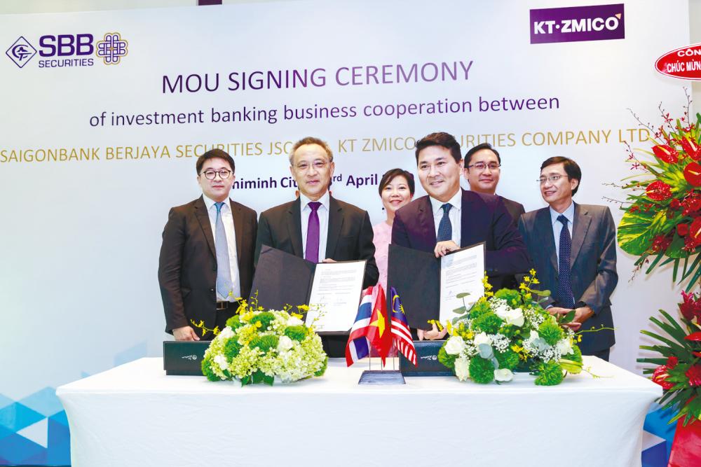 SBBS chairman Nguyen Hoai Nam (front) and KTZ chairman Kraithip Krairiksh exchange documents at the signing ceremony, witnessed by SBBS CEO Josephine Yei (back row, centre) and Consul General of Malaysia to Ho Chi Minh City Sofian Akmal Abd Karim (back row, 2nd from right).