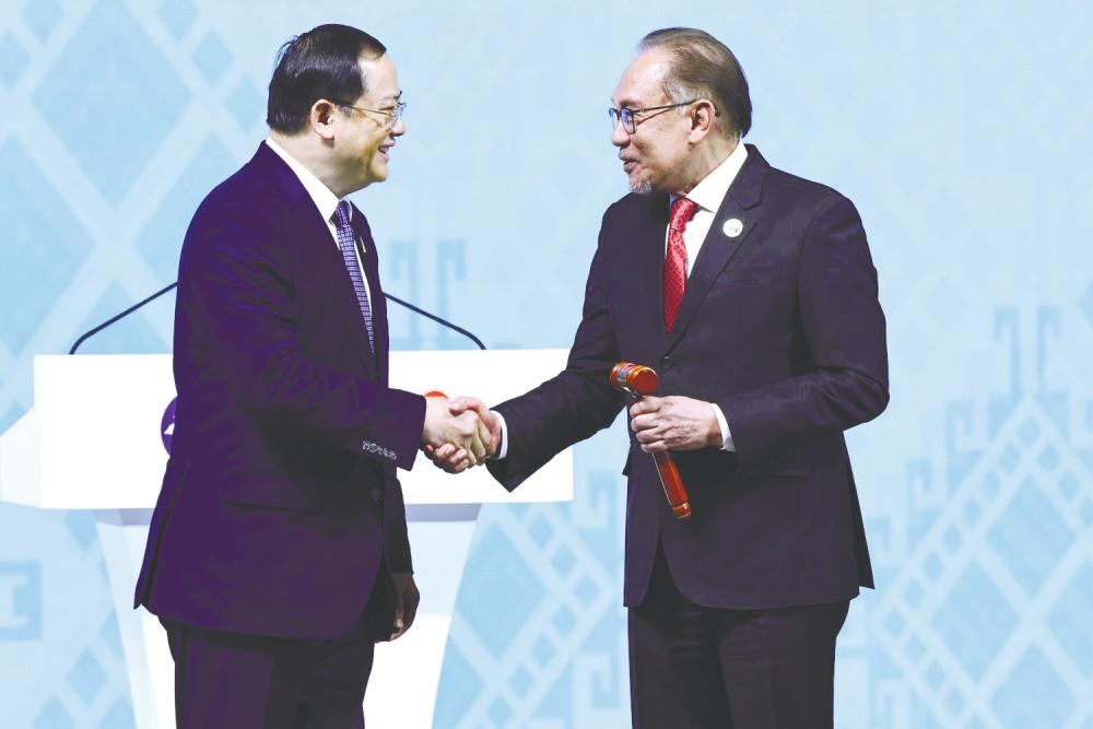 Prime Minister Datuk Seri Anwar Ibrahim holds the ceremonial gavel as he shakes hands with Laos Prime Minister Sonexay Siphandone, who handed over his country’s chairmanship to Malaysia. – REUTERSPIC