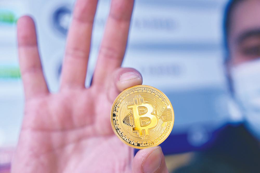 A man holding a physical imitation of a Bitcoin. Cryptocurrencies have been among the big winners this year, with Bitcoin leading the surge with a year-to-date gain of 232.7% as of 10pm yesterday. – AFPPIX