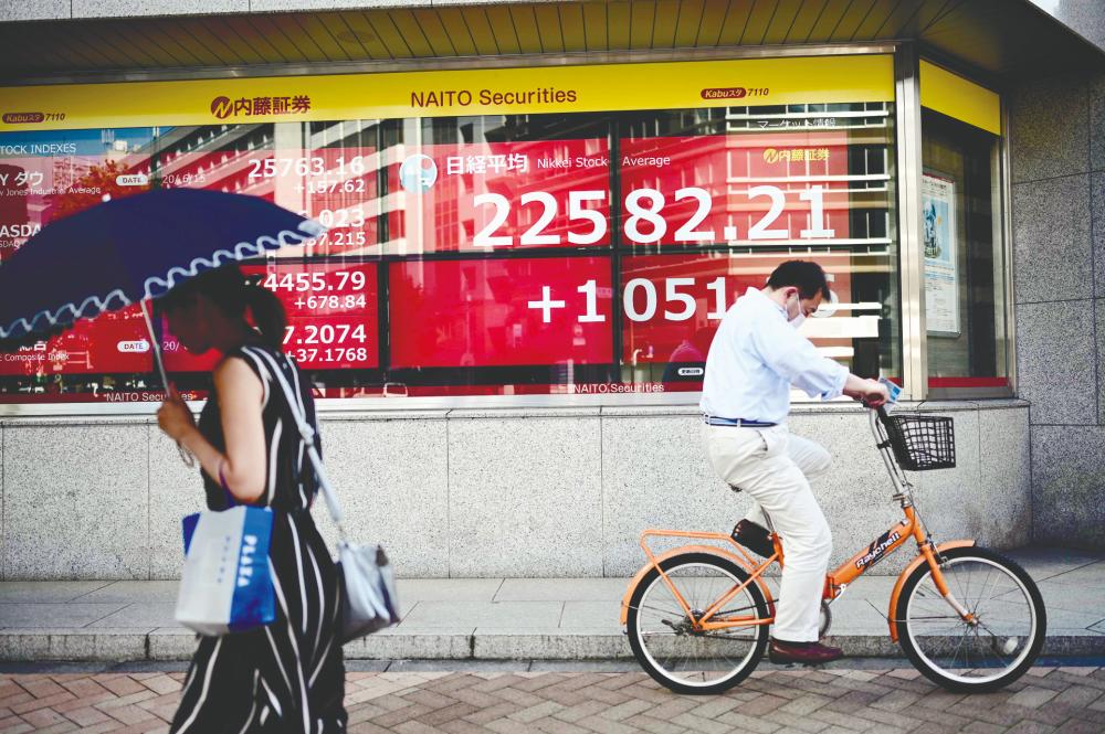 Pedestrians pass by an electronic quotation board displaying closing numbers of the Tokyo Stock Exchange yesterday. Bursa Malaysia’s rally is not an isolated case as regional markets are also propped by liquidity. – AFPPIX