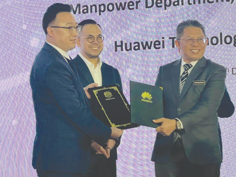 Sim witnessing the exchange of documents between Huawei Malaysia vice-president Michael Zhuang (left) and JTM deputy director-general Kamaruzaman Md Ali.