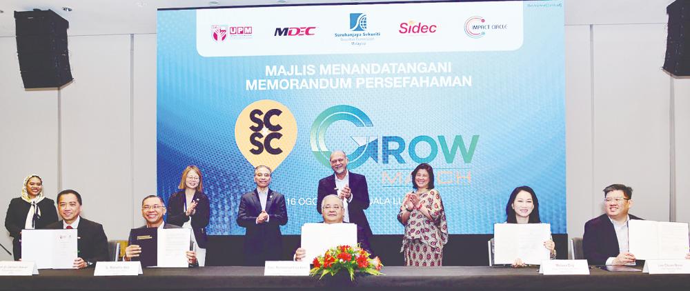 Gobind (standing, second from right) witnessing the signing of the memorandums of understanding by, from left, UPM deputy vice-chancellor Zamberi Sekawi, MDEC CEO Mahadhir Aziz, Mohammad Faiz, Impact Circle deputy CEO Melissa Ong and Sidec CEO Loo Chuan Boon.