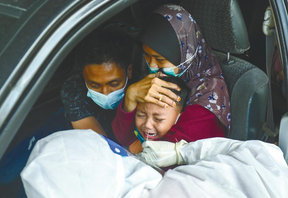 $!A COMFORT CUDDLE ... A boy is embraced by his dotting parents as a health worker inserts a nasal swab into his nostril during a free screening drive in Subang Jaya, Selangor yesterday. – ASYRAF RASID/THESUN