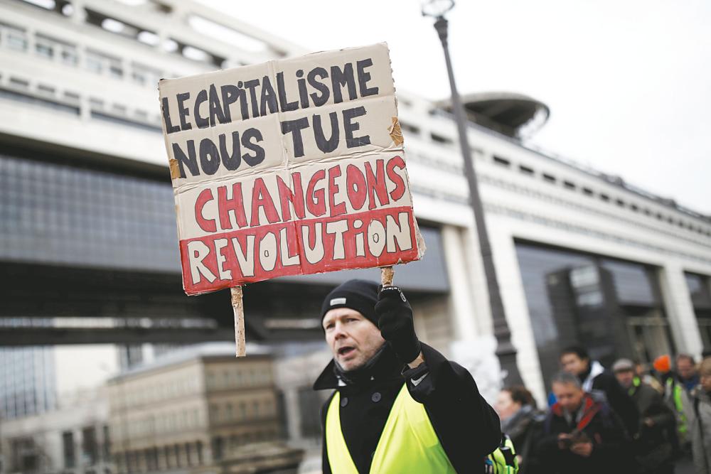 A protester wearing a yellow vest holds a placard reading “Capitalism is killing us” in front of France’s Finance Ministry during the movement’s 56th round of protests with a backdrop of social discontentment triggered by president Macron’s pensions reform plan in Paris on Saturday. – Reuterspix