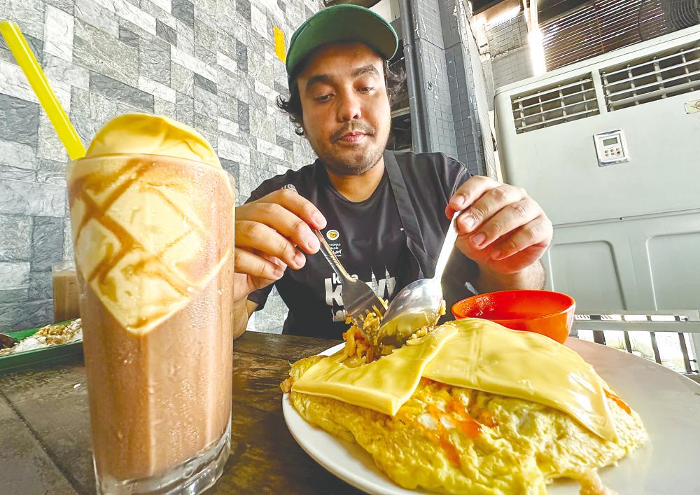 A diner enjoying a serving of cheese-topped ‘Nasi Goreng Pattaya’ and a glass of iced Milo with cheese slices. - Adib Rawi Yahya/theSun