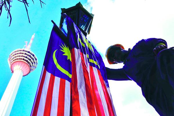 $!MERDEKA SPIRIT ... A worker hanging the Jalur Gemilang on a lamp post near the Kuala Lumpur Tower yesterday in preparation for the Merdeka month. – ZAHID IZZANI/THESUN