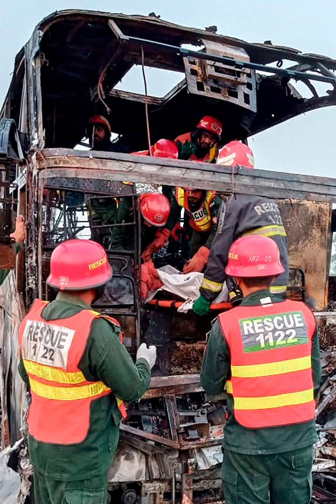 This handout photograph taken and released by Pakistan’s Emergency Rescue 1122 Service on August 20, 2023 shows rescue workers carrying a victim’s body from a burned passenger bus at the site after a accident on a highway near the town of Pindi Bhattian in eastern Punjab province. AFPPIX