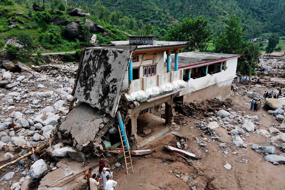 An aerial view shows flood survivors standing near a damaged house surrounded by heavy rocks in the Buner district of mountainous Khyber Pakhtunkhwa province on August 17, 2025. - Abdul MAJEED / AFP