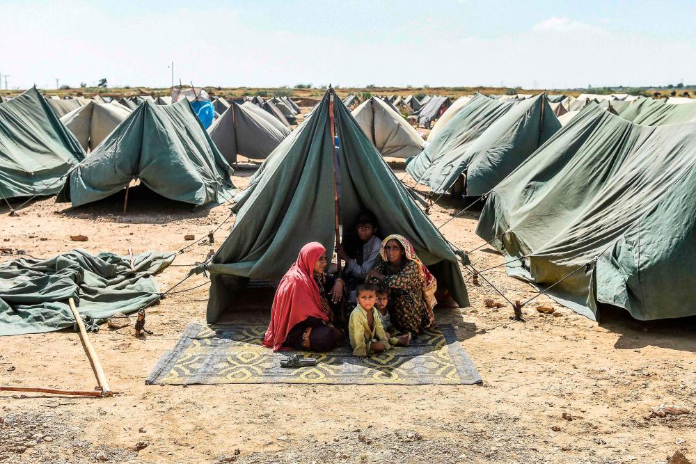 In this picture taken on September 28, 2022, an internally displaced flood-affected family sits outside their tent at a makeshift tent camp in Jamshoro district of Sindh province. AFPPIX
