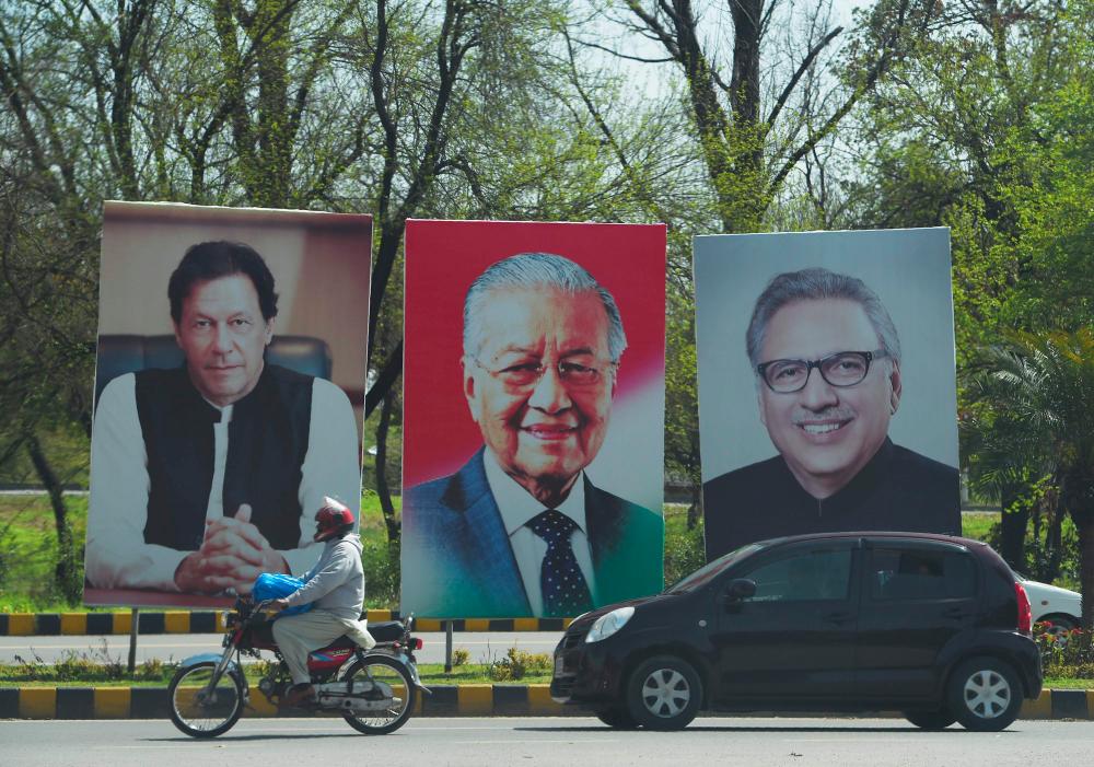 Pakistani peoples ride past the portraits of Prime Minister Imran Khan (L), President Airf Alvi (R) along with Malaysia's Prime Minister Mahathir Mohamad (C) on the Constitution avenue in Islamabad on March 21, 2019. — AFP