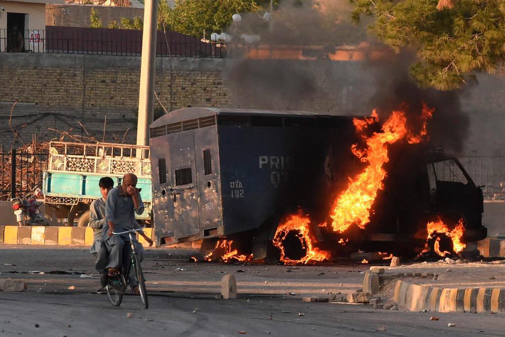 Men on a bike ride past a burning police vehicle during a protest by Pakistan Tehreek-e-Insaf party activists and supporters of former Pakistan’s Prime Minister Imran against the arrest of their leader, in Quetta on May 9, 2023/AFPpix