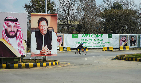 A foreigner rides past billboards showing portraits of Saudi Arabian Crown Prince Mohammed bin Salman (L) and Pakistan’s Prime Minister Imran Khan (R) and a banner welcoming the prince ahead of his arrival in Islamabad on Feb 15, 2019. — AFP