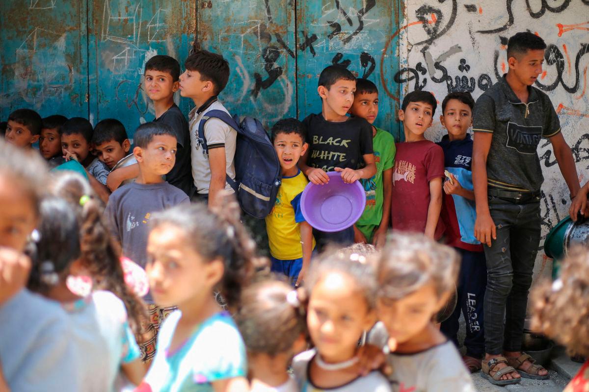 Palestinians queue at a food distribution point in Nuseirat, in the central Gaza Strip, on June 23, 2025. The Israeli blockade imposed in early March amid an impasse in truce negotiations had produced famine-like conditions across Gaza, according to rights groups. (Photo by Eyad BABA / AFP)