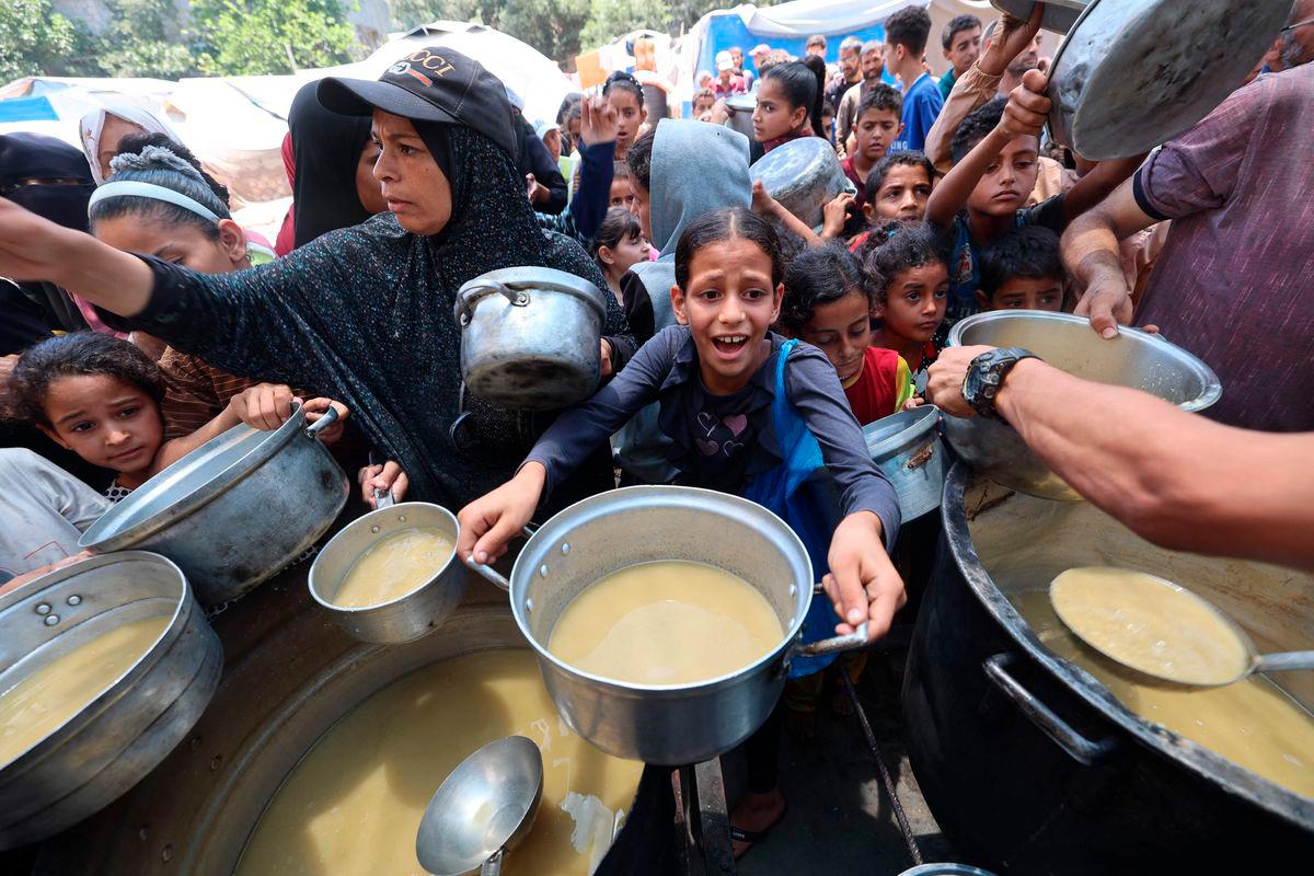 Palestinian children line up to receive a hot meal at a food distribution point in Nuseirat on June 30, 2025. (Photo by Eyad BABA / AFP)
