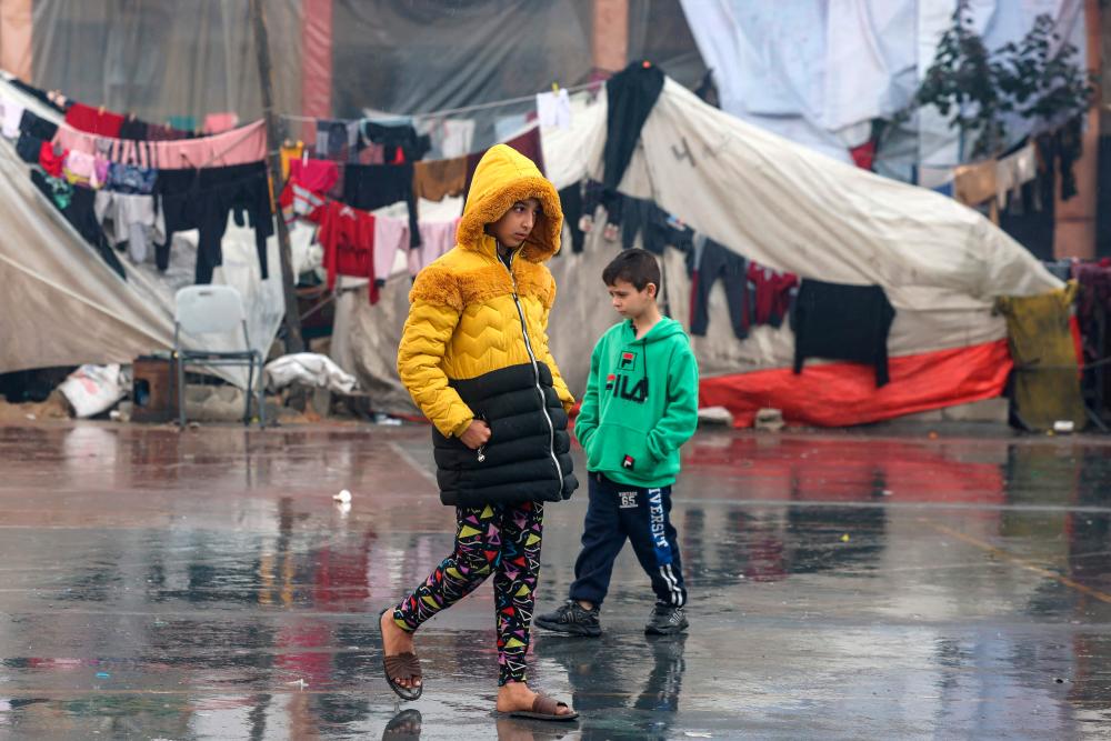 Palestinians children walk near makeshift tents at a camp set up on a schoolyard in Rafah in the southern Gaza Strip where most civilians have taken refuge, on December 13, 2023, as battles continue between Israel and the Palestinian militant group Hamas/AFPPix