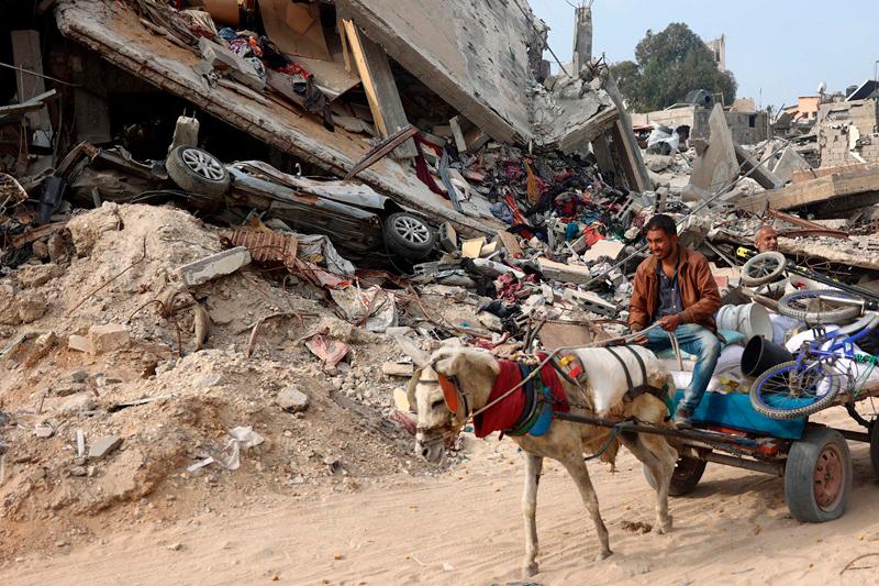 A Palestinian man rides a horse-pulled cart, next to a destroyed building where personal belongings of people and a car are sandwiched between the layers of its rubble, in Gaza City on November 2, 2024, amid the ongoing war between Israel and Hamas militants. (Photo by Omar AL-QATTAA / AFP)