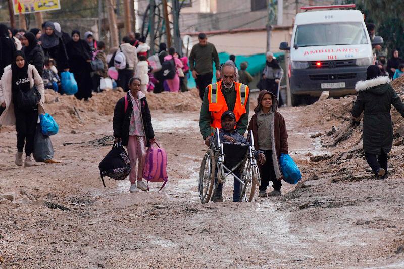 People carrying their belongings use a street previously destroyed by Israeli forces as they flee the Jenin refugee camp in the occupied West Bank with assistance from the Palestinian Red Crescent on January 23, 2025, days into a large-scale Israeli army raid in the area. - MOHAMMAD MANSOUR / AFP