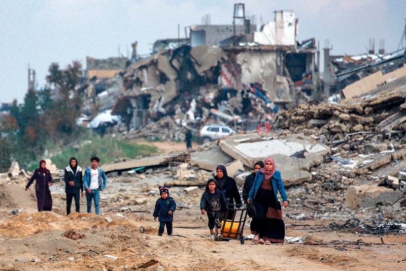 Women and children walk along a destroyed road past collapsed buildings in the west of Beit Lahia in the northern Gaza Strip on February 11, 2025 amid the current ceasefire deal in the war between Israel and Hamas. - BASHAR TALEB / AFP