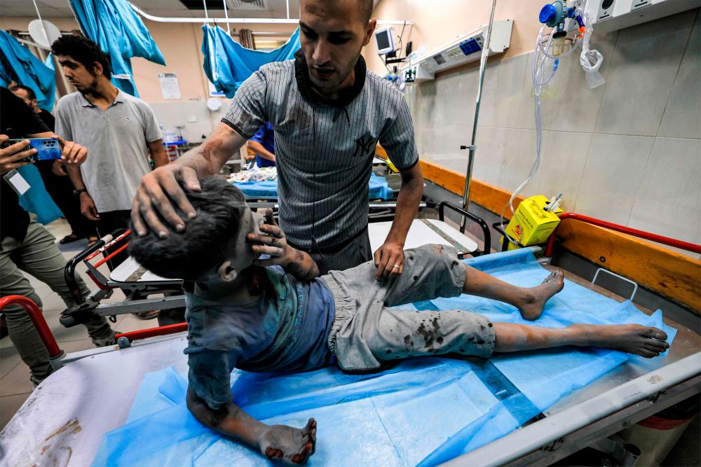 A man checks on a child who was injured in Israeli bombardment while waiting on a hospital bed for emergency treatment at a trauma ward at Nasser hospital in Khan Yunis in the southern Gaza Strip on October 24, 2023. AFPPIX