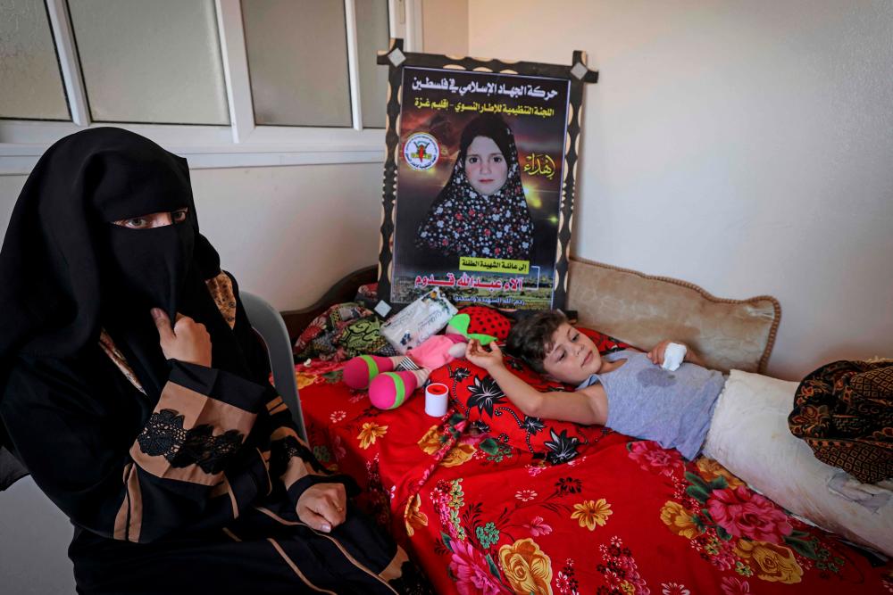 Palestinian mother Rasha Qadoom sits by her wounded child Rayed near a poster depicting her five-year-old daughter Alaa killed during the latest conflict between Israel and Palestinian militants, in Gaza on August 9, 2022. AFPPIX