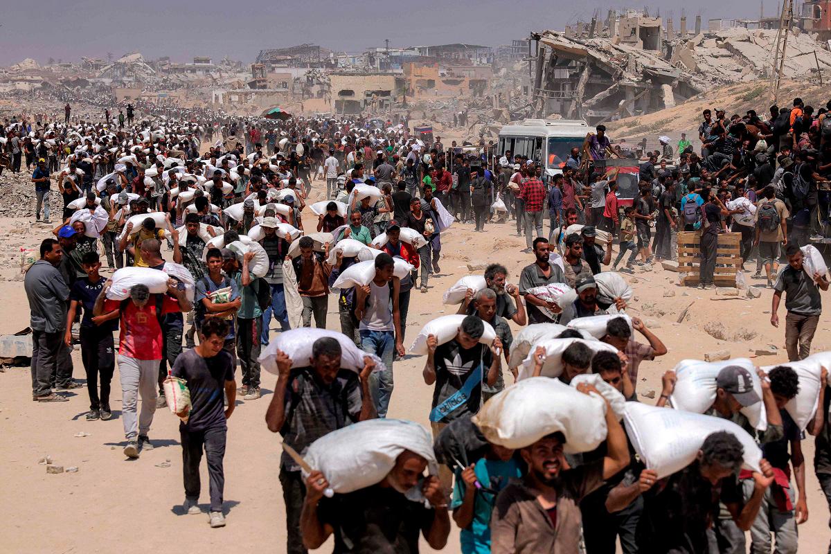 People walk with sacks of flour delivered after trucks carrying humanitarian aid entered northern Gaza on July 27, 2025 coming from the Zikim border crossing. - BASHAR TALEB / AFP