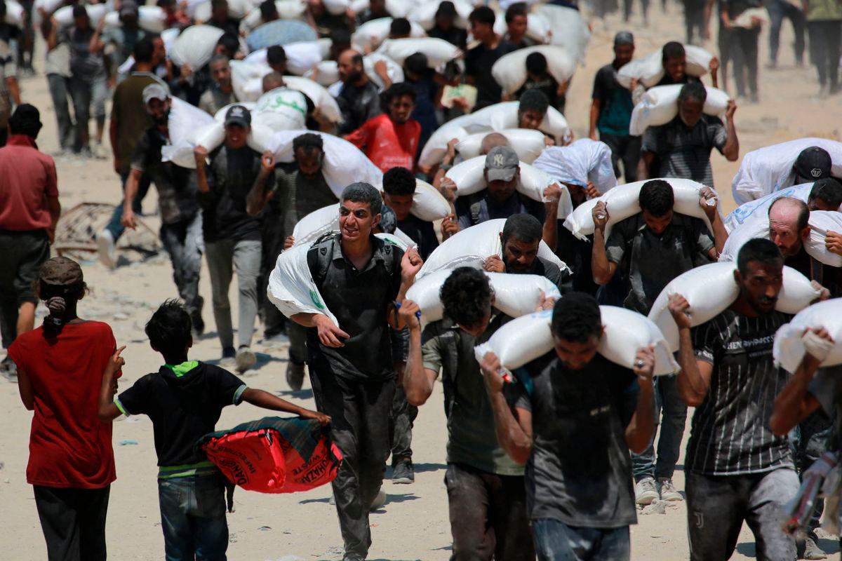Palestinian walk carrying sacks of flour near Jabalia, in the northern Gaza Strip, on July 27, 2025, after planes dropped aid into Gaza. (Photo by BASHAR TALEB / AFP)