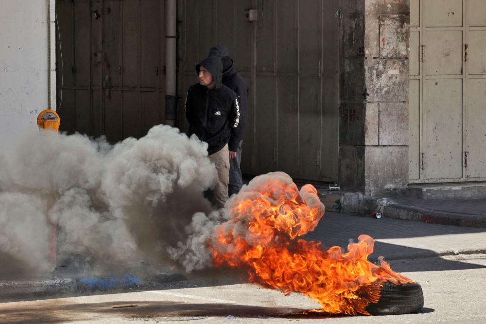 Palestinian youths stand behind burning tyre during clashes with Israeli forces following the death announcement of a Palestinian hunger striker who was in Israeli detention, on May 2, 2023, in Hebron, in the occupied West Bank. AFPPIX