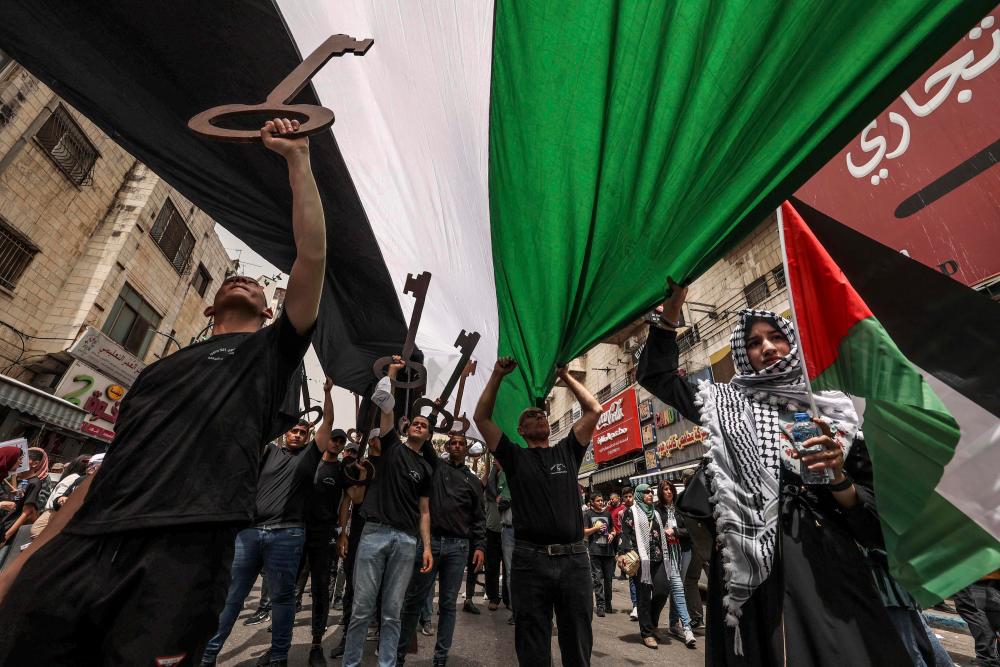 Palestinian wave national flags and carry giant mock keys (a widely used symbol of the Nakba, as many Palestinians kept the keys to their homes when they were forced into exile in 1948), as they march in a rally marking the 74th anniversary of the “Nakba” or “catastrophe”, in the occupied West Bank town of Ramallah, on May 15, 2022. AFPPIX
