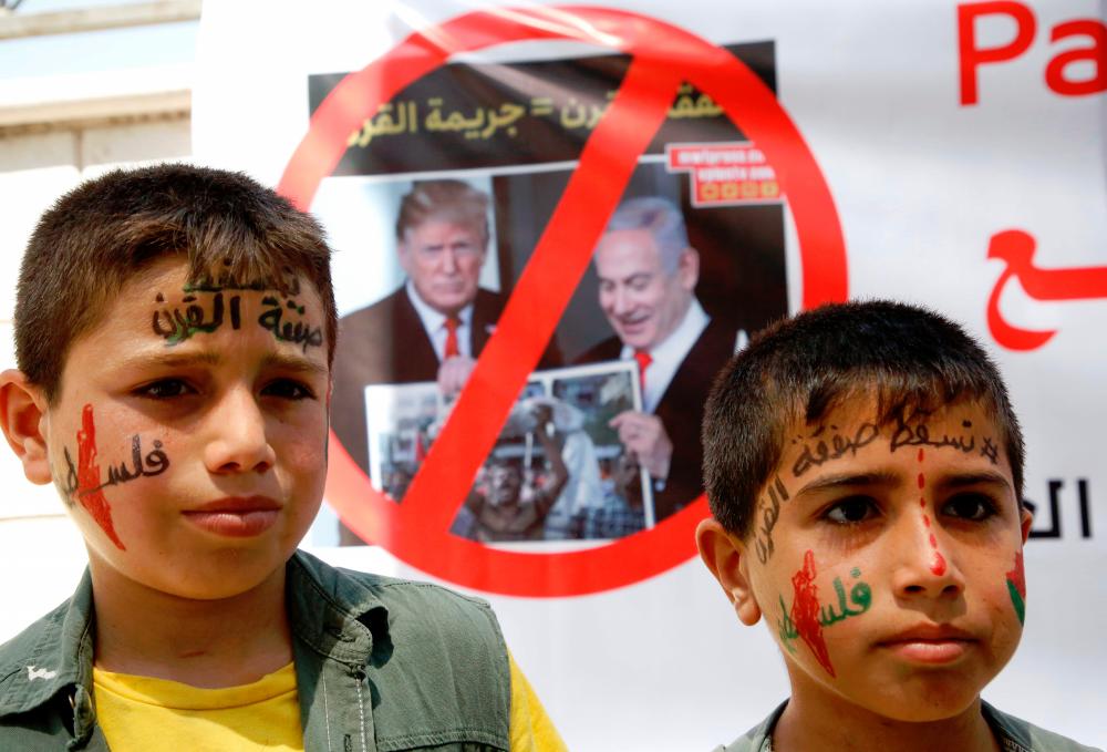 Palestinian children stand in front of a banner bearing the crossed out images of President Donald Trump and Israeli Prime Minister Benjamin Netanyahu during a protest against a US-led meeting this week in Bahrain on the Palestinian-Israeli conflict, in the village of Yatta near the West Bank city of Hebron, on June 24, 2019. — AFP