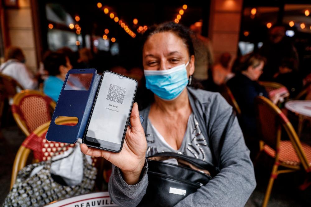 A woman shows her health pass at a coffee shop in Deauville on July 27, 2021. France's highest constitutional authority said on July 26, 2021 it would rule next week on new legislation passed by parliament that would make vaccine passes a key part of daily life. -AFP