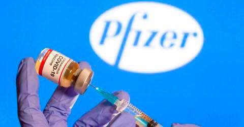 A woman holds a small bottle labeled with a “Coronavirus Covid-19 Vaccine” sticker and a medical syringe in front of displayed Pfizer logo in this illustration taken, October 30, 2020. — Reuters