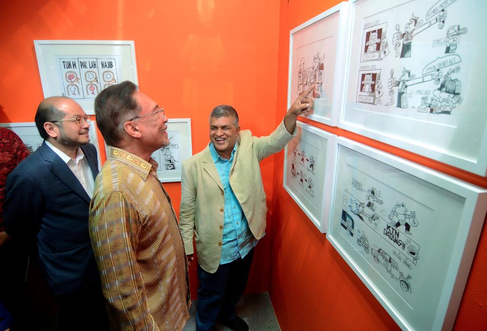 Cartoonist Zukiflee Anwar Haque (R) shows his work to PKR president Datuk Seri Anwar Ibrahim (C) at the officiation of Art Of Freedom By Zunar exhibition at George Town on May 5, 2019. — Bernama